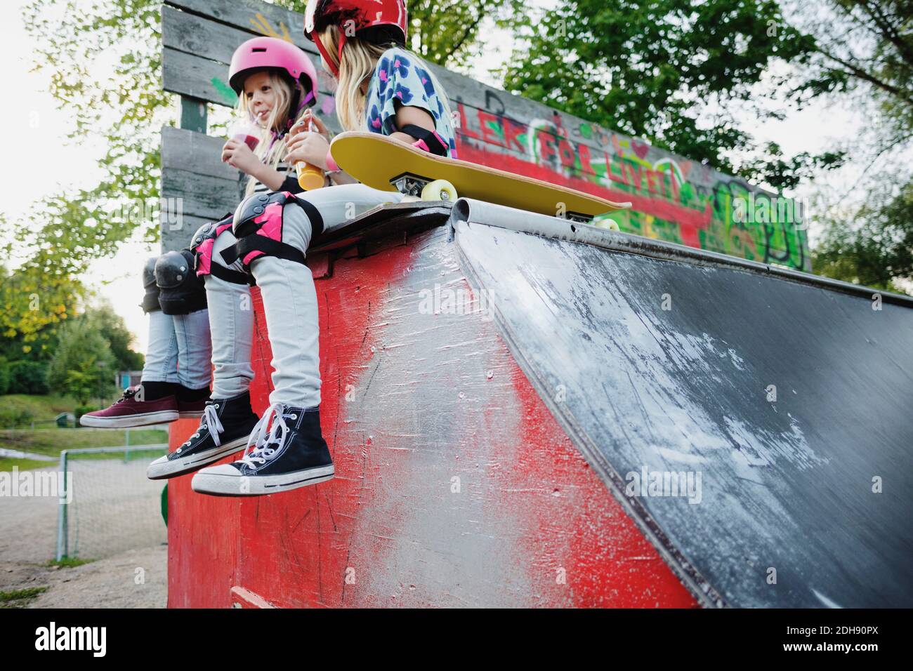 Low angle view of friends drinking juice while sitting on edge of skateboard ramp Stock Photo