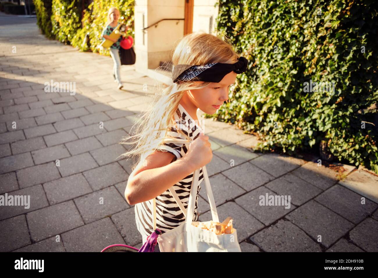 Girl carrying while walking on sidewalk during sunny day Stock Photo