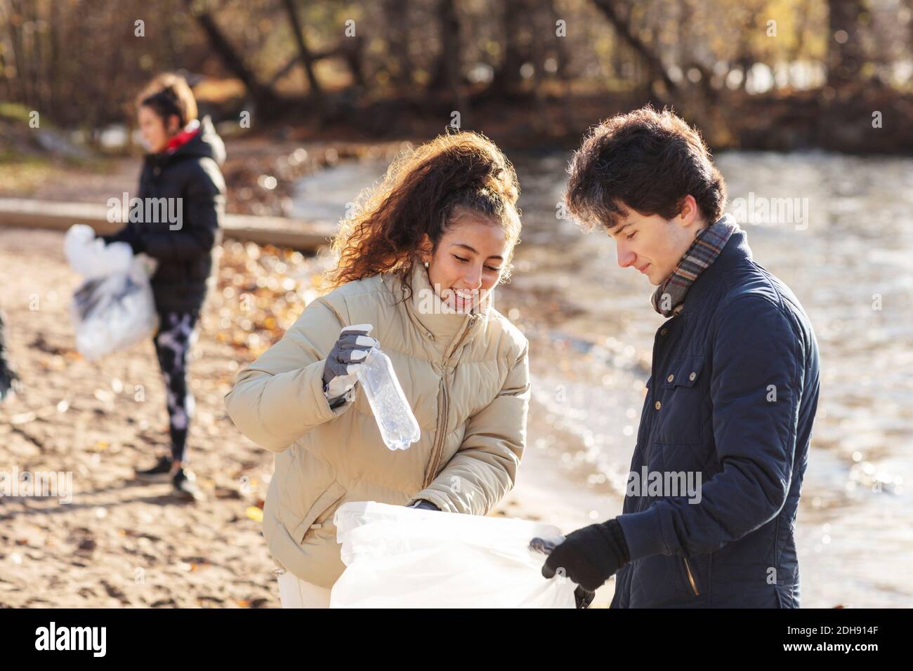 Smiling female volunteer with male friend holding plastic bottle in garbage bag Stock Photo