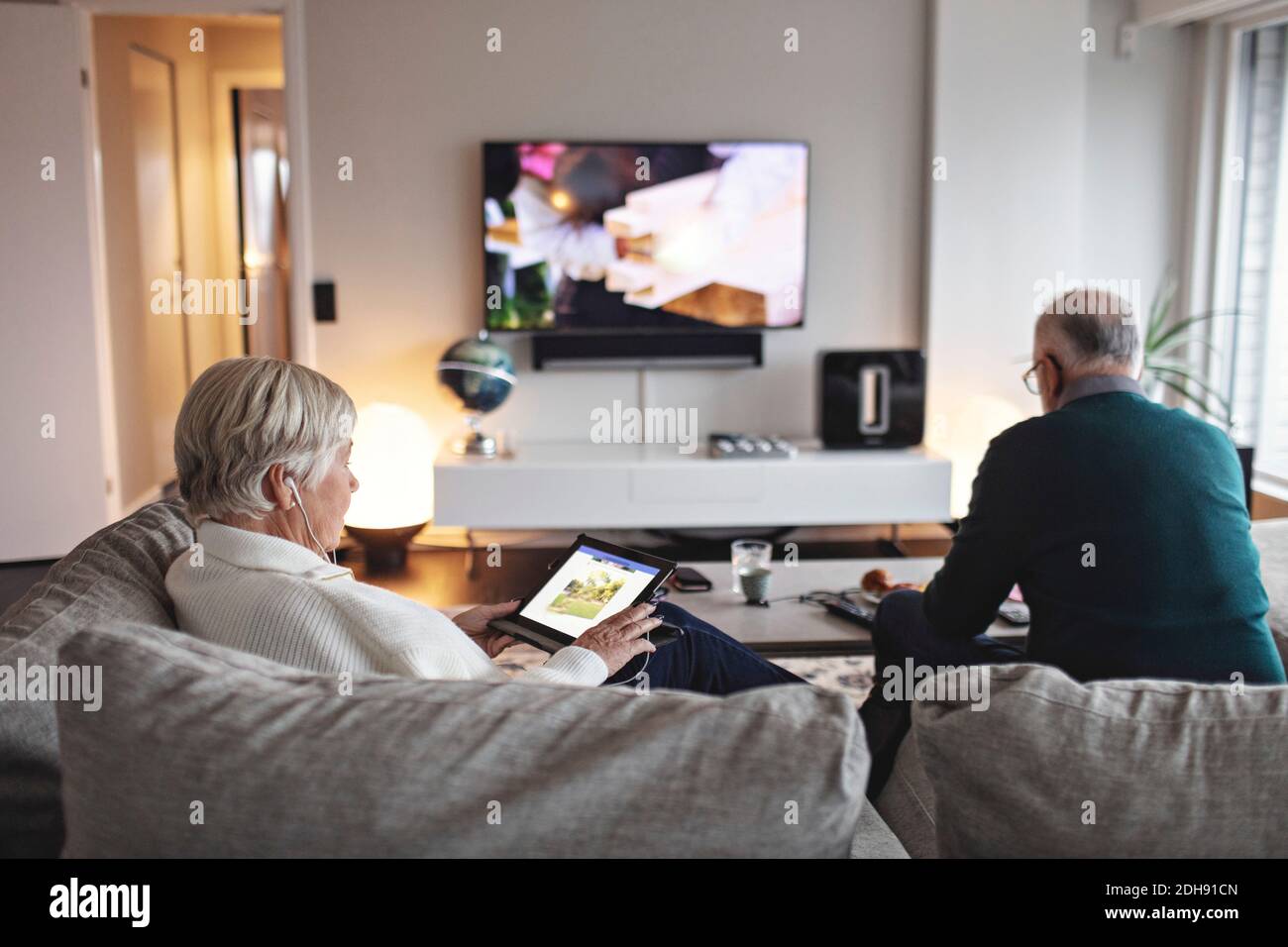 Senior woman using digital tablet while partner sitting on sofa in living room Stock Photo
