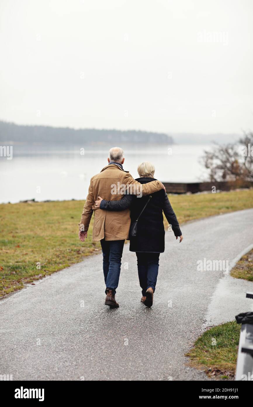 Rear view of senior couple with arm around walking on footpath during winter Stock Photo