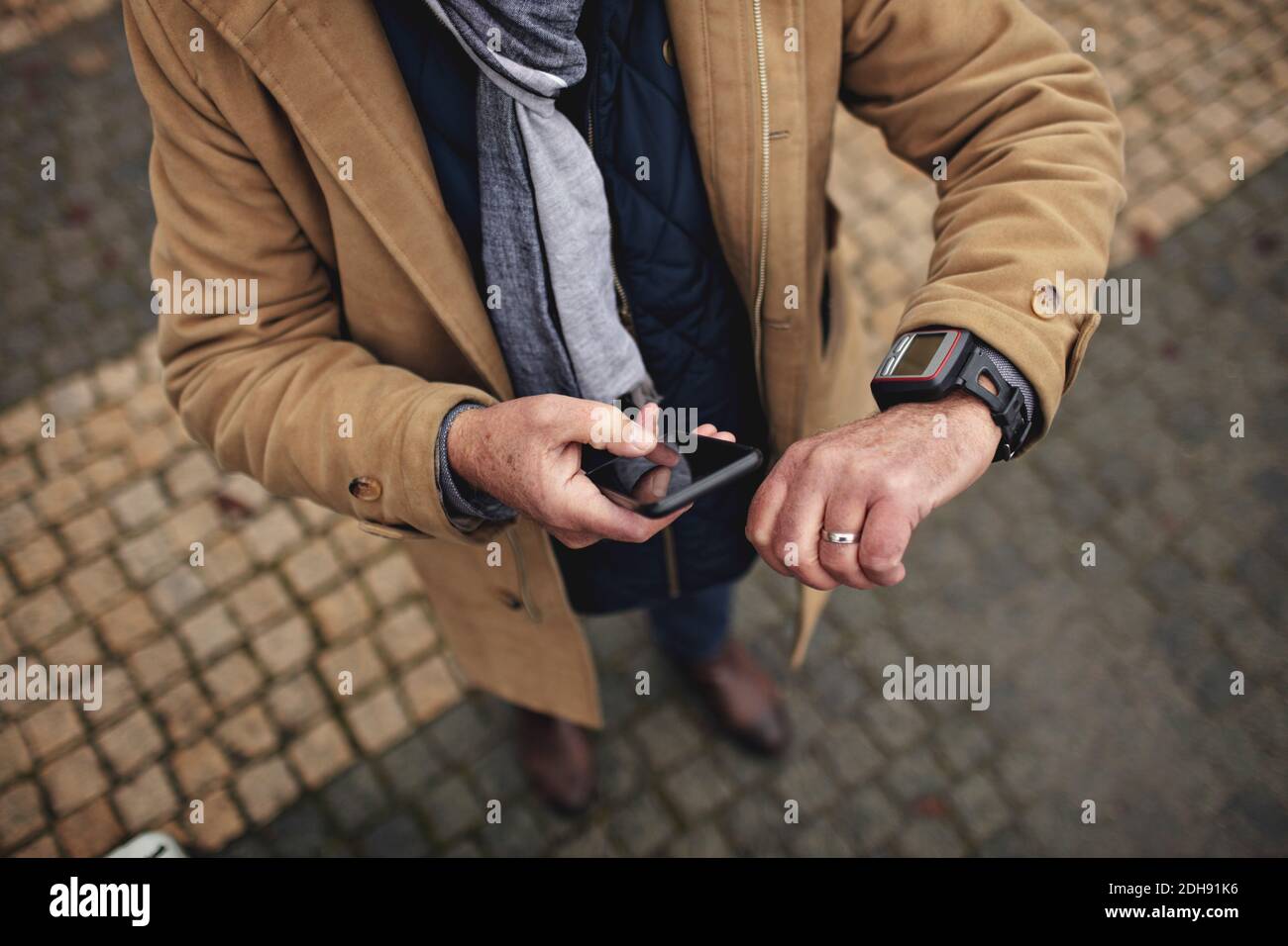 Low section of man using phone while checking the time on footpath Stock Photo
