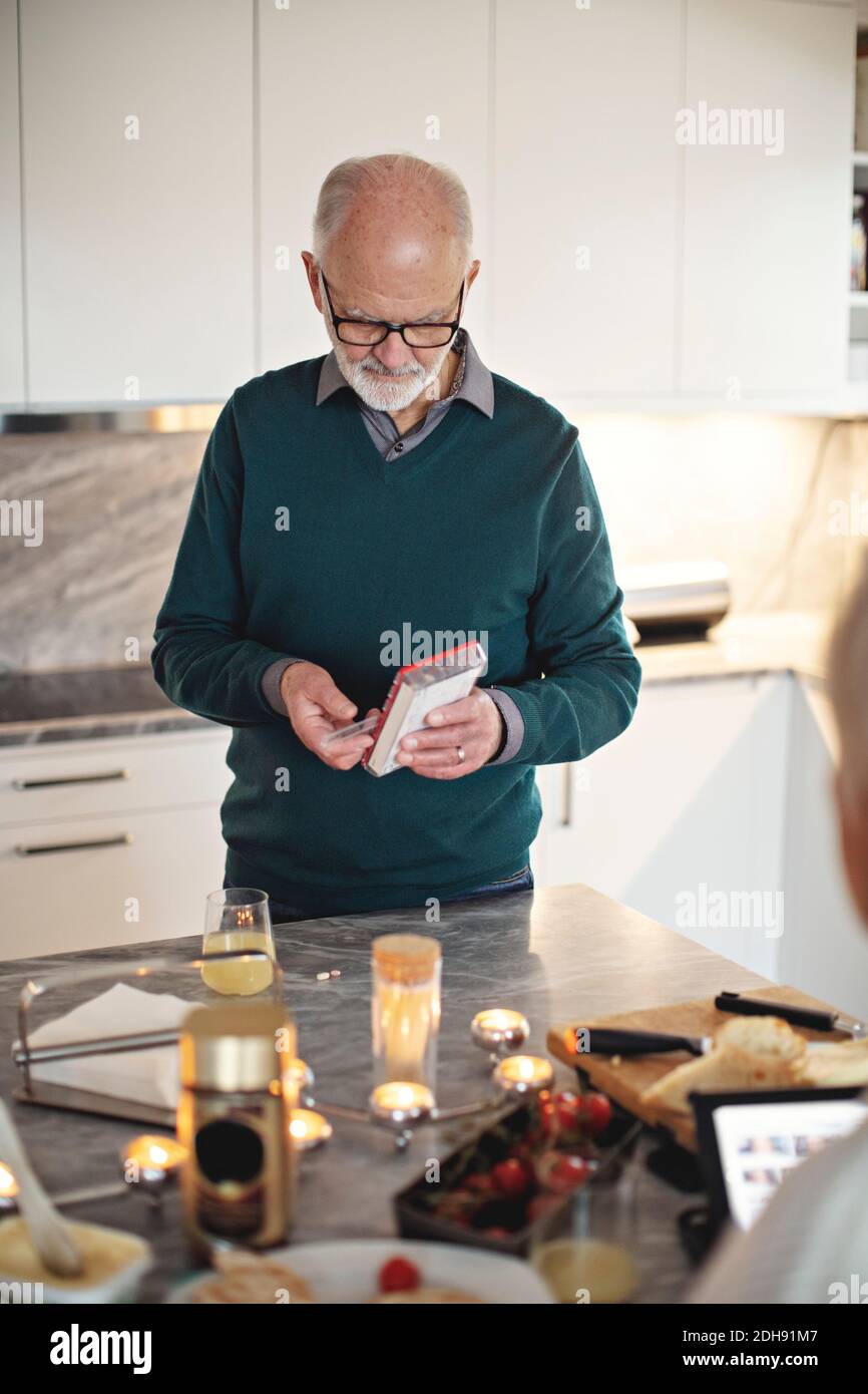 Senior man taking pills while standing by kitchen island at home Stock Photo