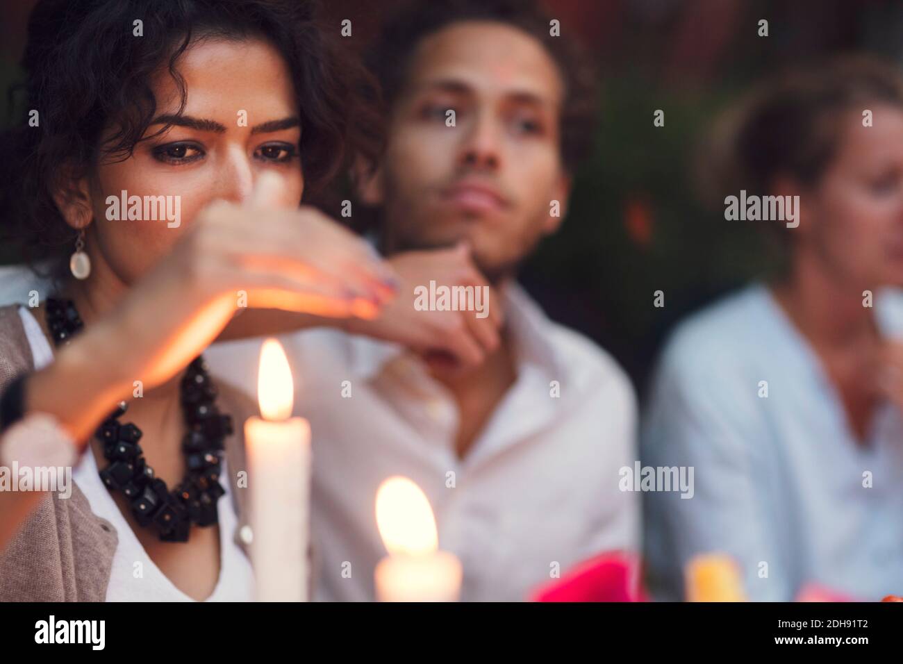 Woman covering candle while sitting with friends at garden party Stock