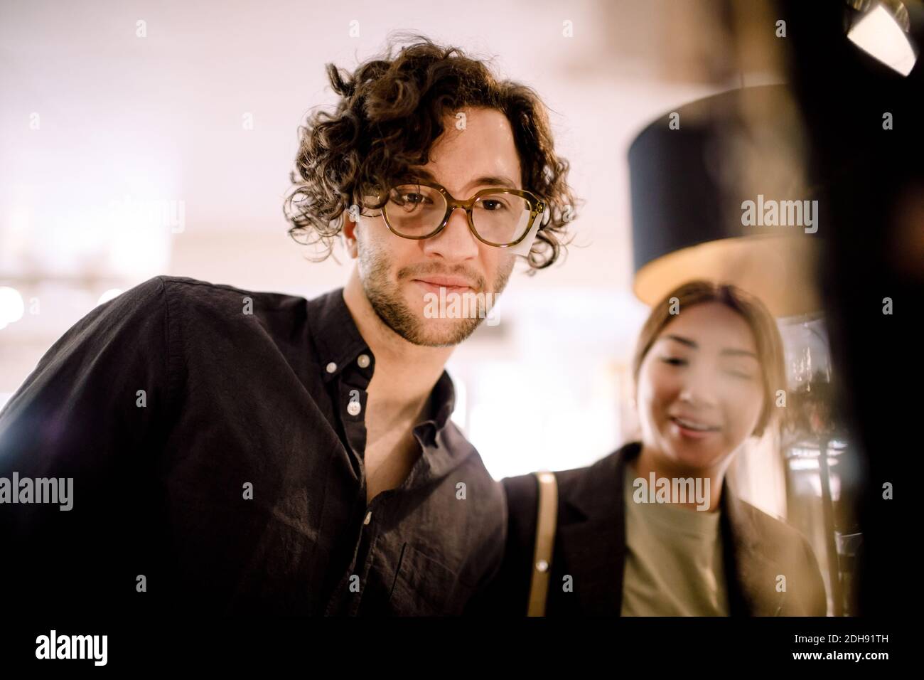 Smiling man trying fashionable eyeglasses with friend at store Stock Photo