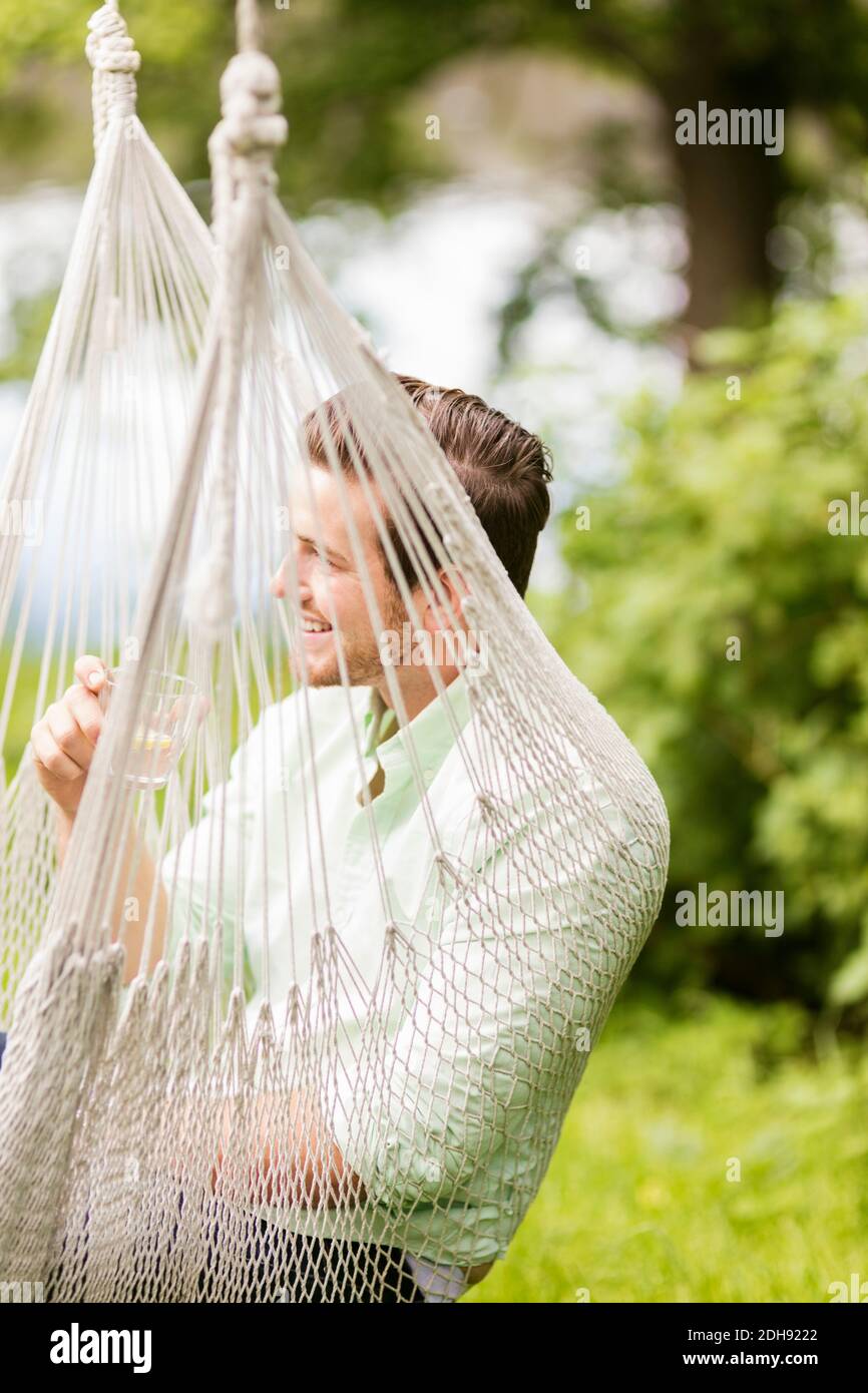 Smiling man having drink while resting in hammock Stock Photo