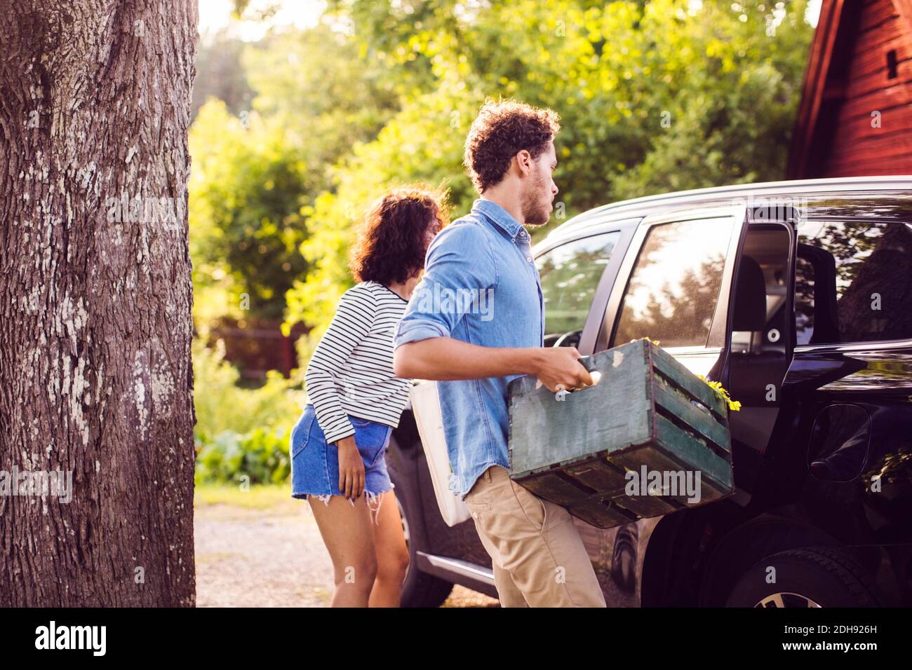 Man holding crate while standing with woman by car on sunny day Stock Photo