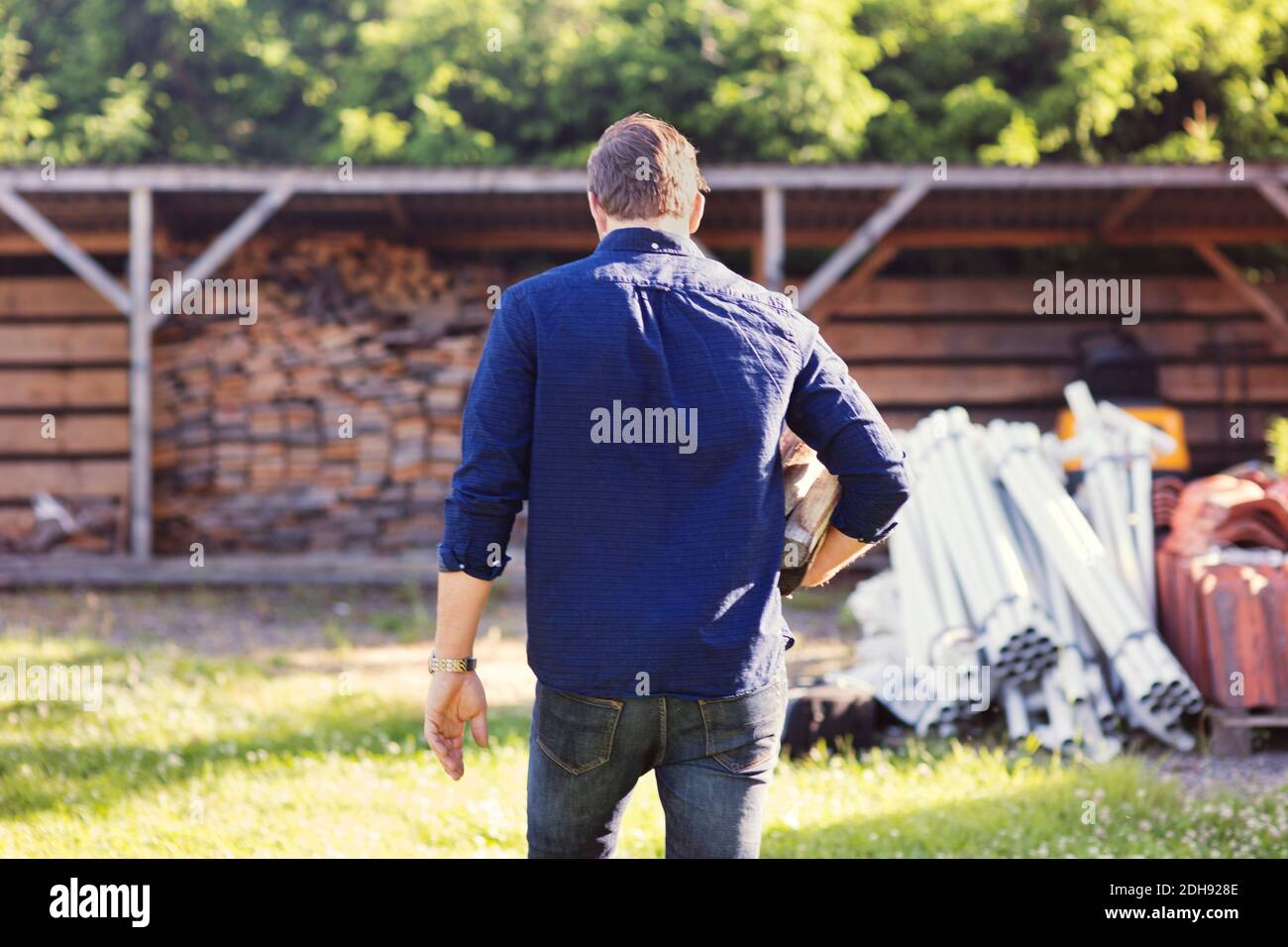 Rear view of man carrying firewood while walking towards shed Stock Photo
