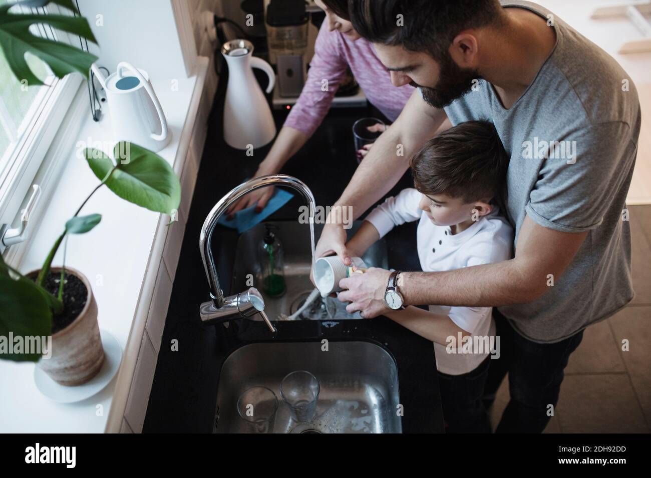 High angle view of father and son washing dishes by woman cleaning counter in kitchen Stock Photo