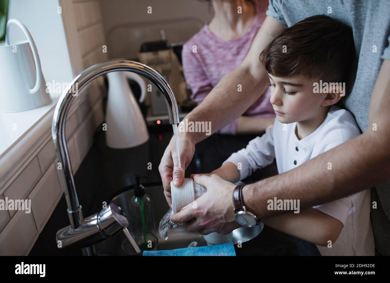 Midsection of man assisting boy in washing dishes by woman in kitchen Stock Photo