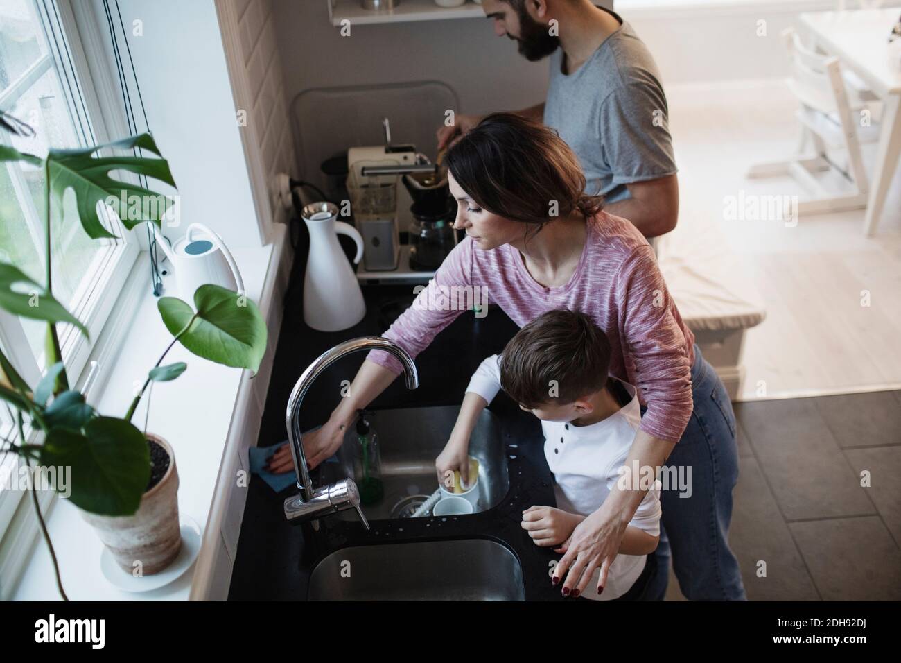 High angle view of man standing by woman cleaning counter while boy washing dishes in kitchen Stock Photo