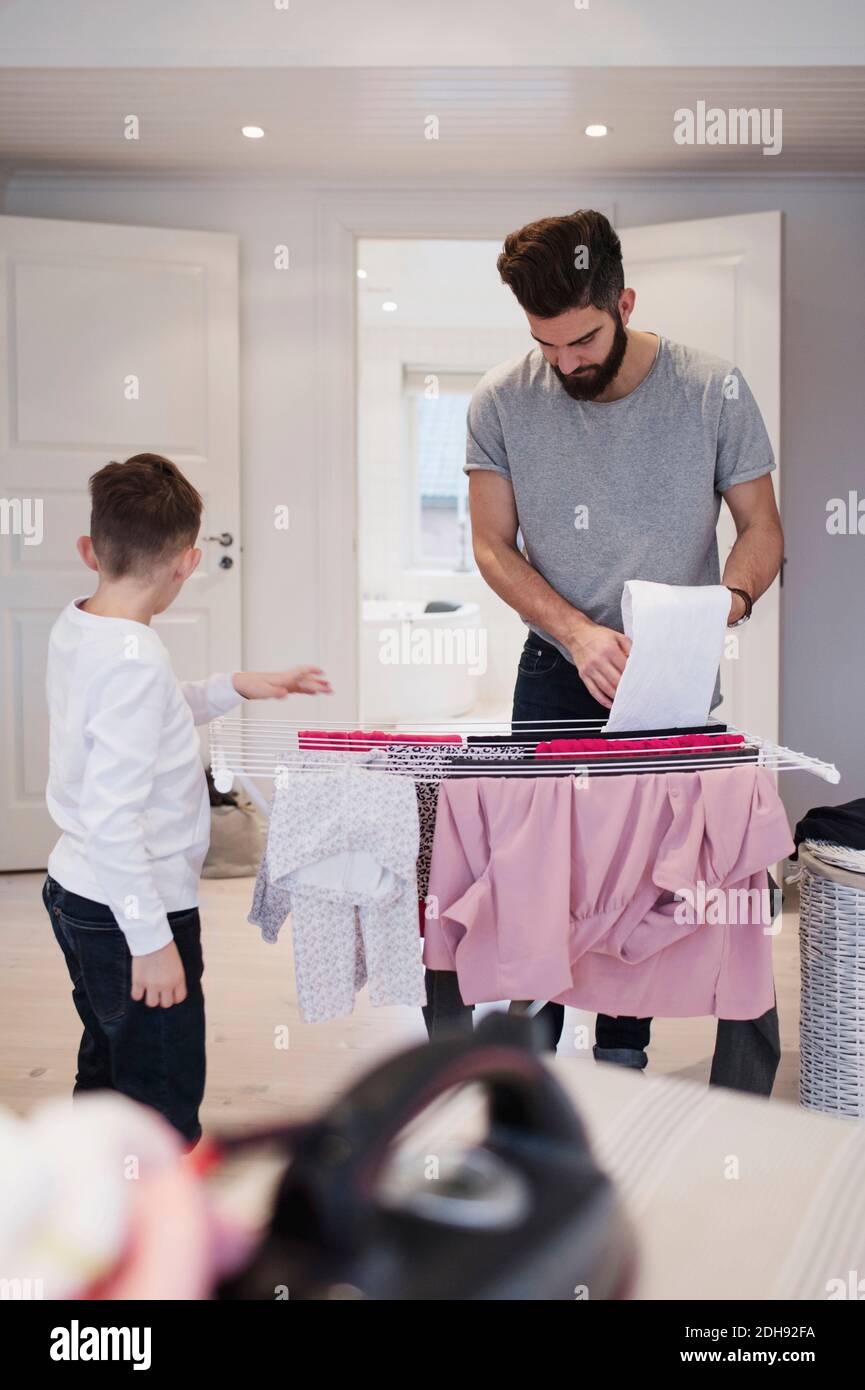 Boy standing by father drying clothes on rack at home Stock Photo