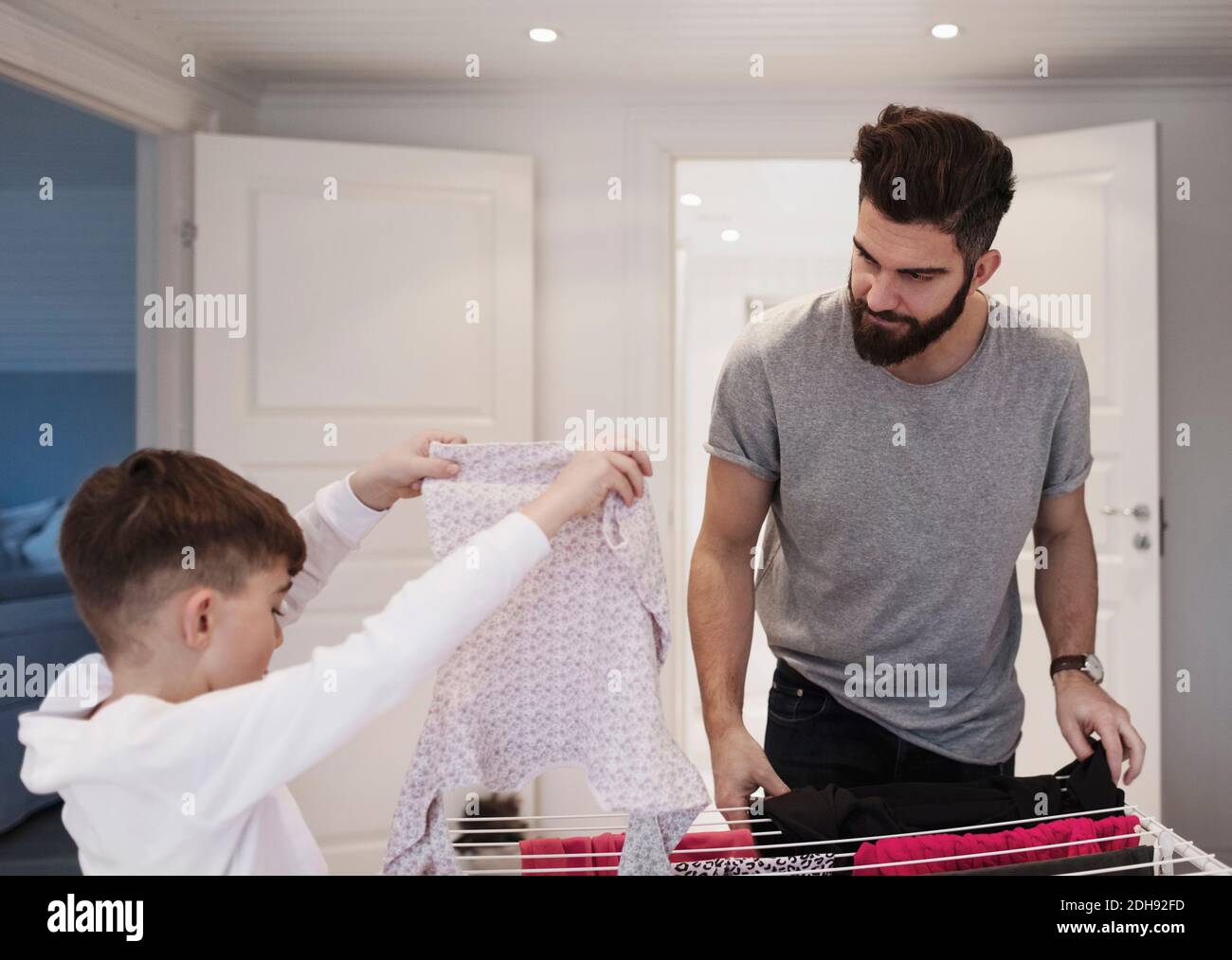 Father looking at boy drying clothes at home Stock Photo