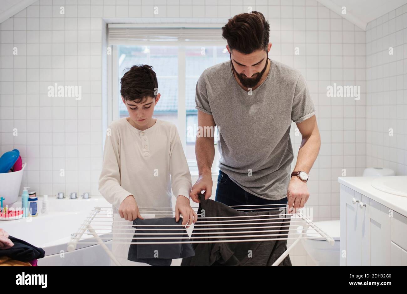 Father and son drying clothes on rack at home Stock Photo