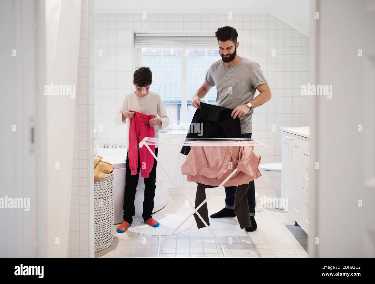 Son and father drying clothes on rack at home Stock Photo