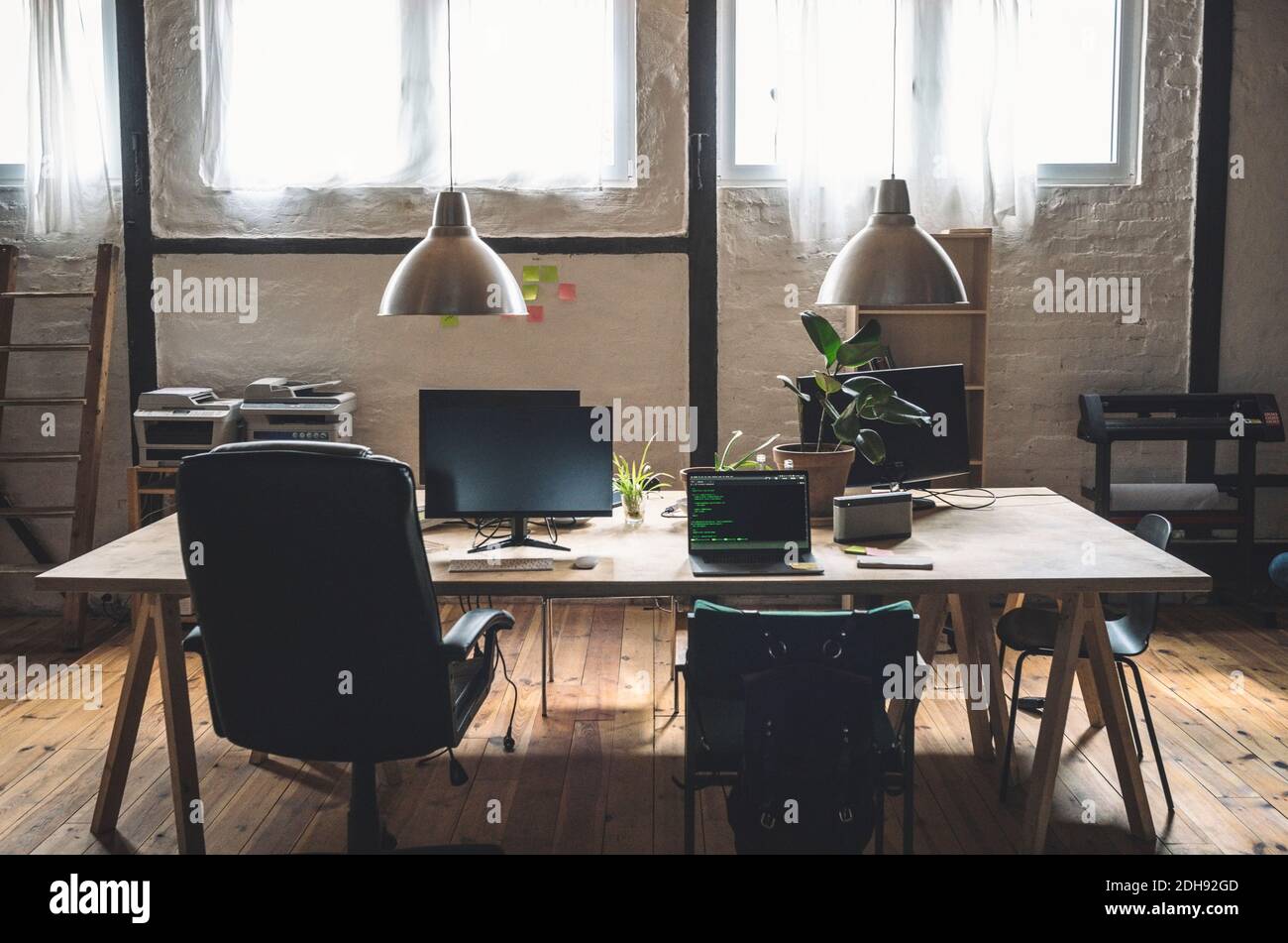 Laptop and computer arranged on table by chairs at workplace Stock Photo