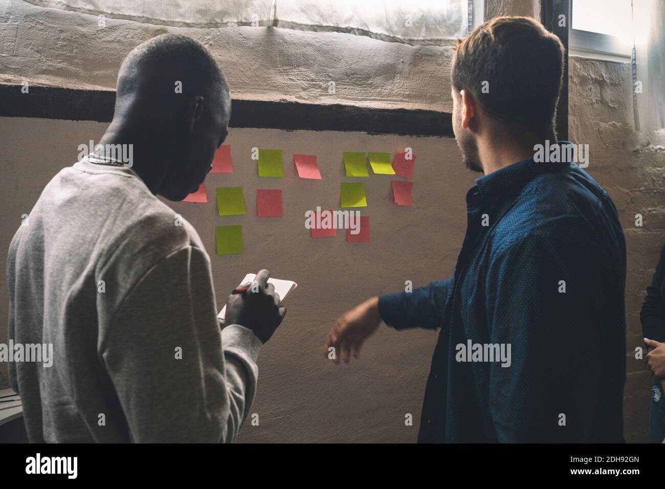 Male coworkers sticking notes on wall at workplace Stock Photo