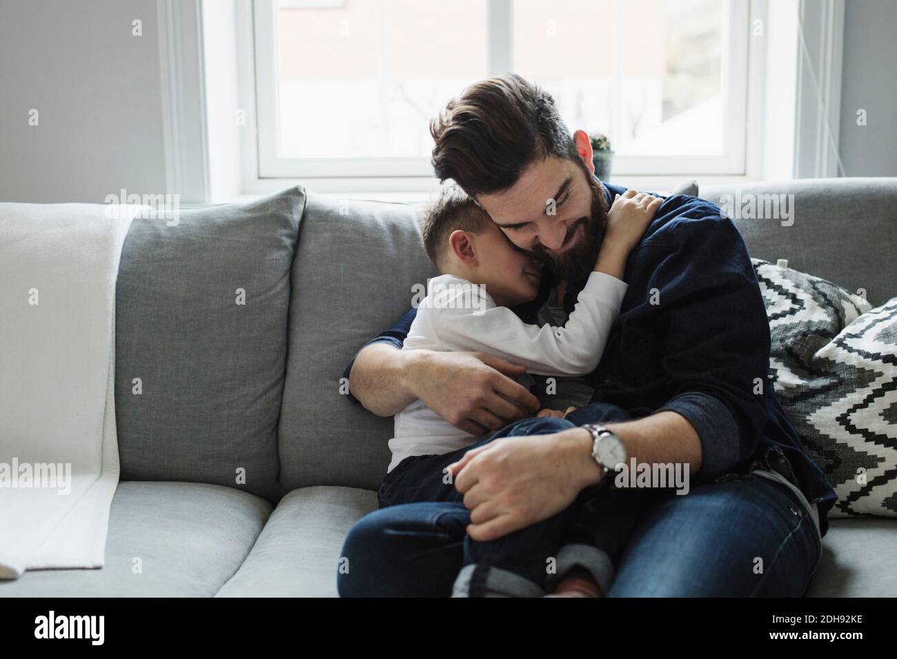 Father embracing son while sitting on sofa at home Stock Photo