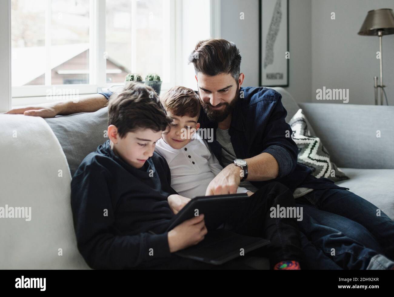 Father and sons using tablet while sitting on sofa at home Stock Photo