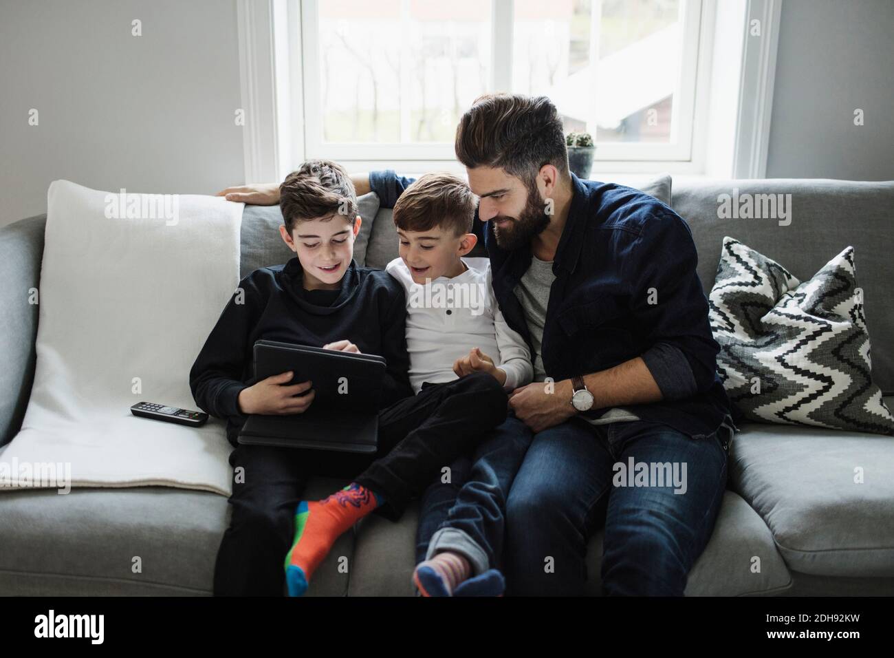 Father and son looking at boy using digital tablet while sitting on sofa Stock Photo