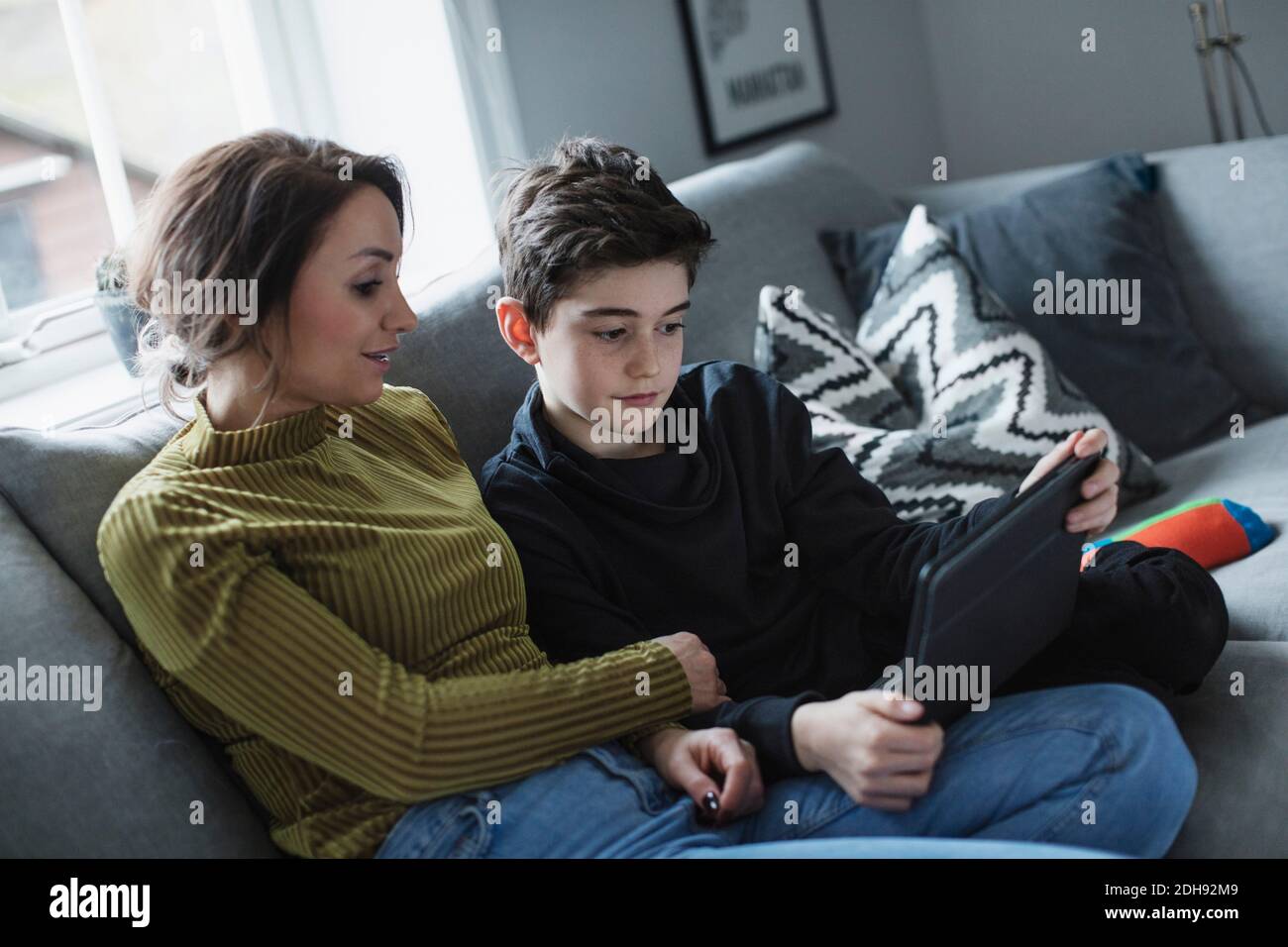 Mother looking at boy using digital tablet while sitting on sofa in living room Stock Photo