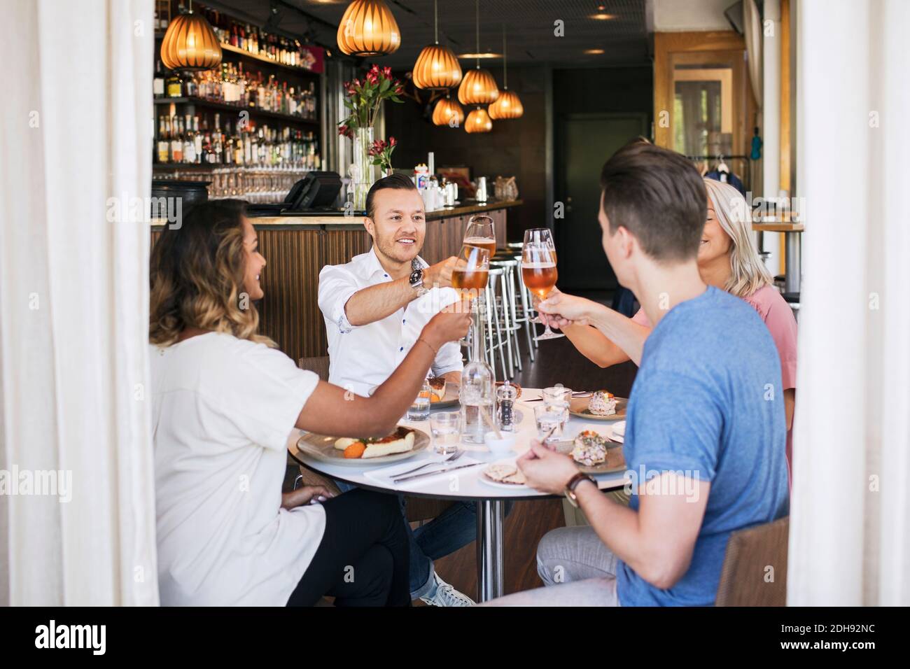 Happy friends raising toast while sitting in restaurant Stock Photo