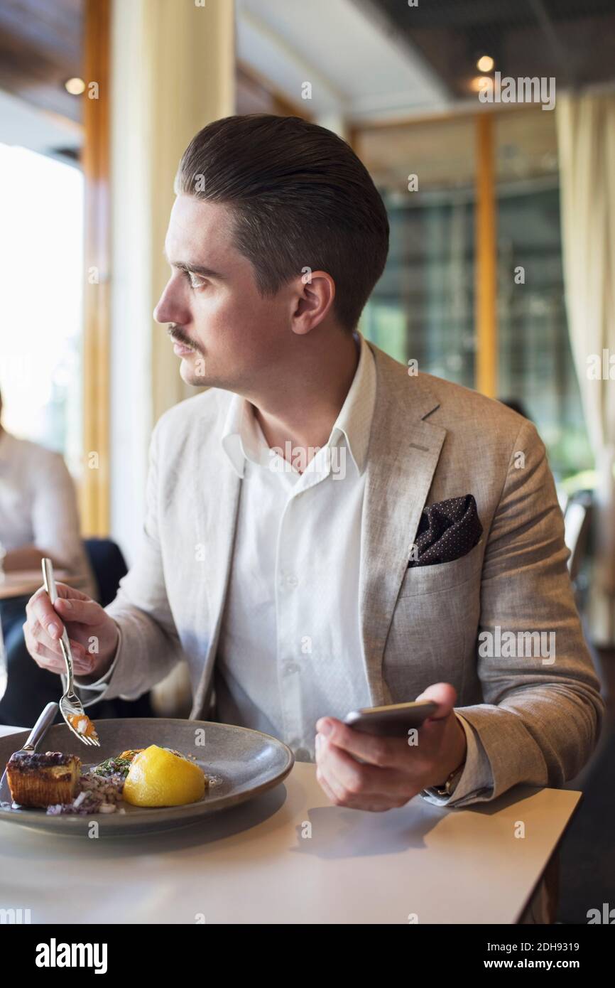 Businessman using mobile phone while looking away at restaurant Stock Photo