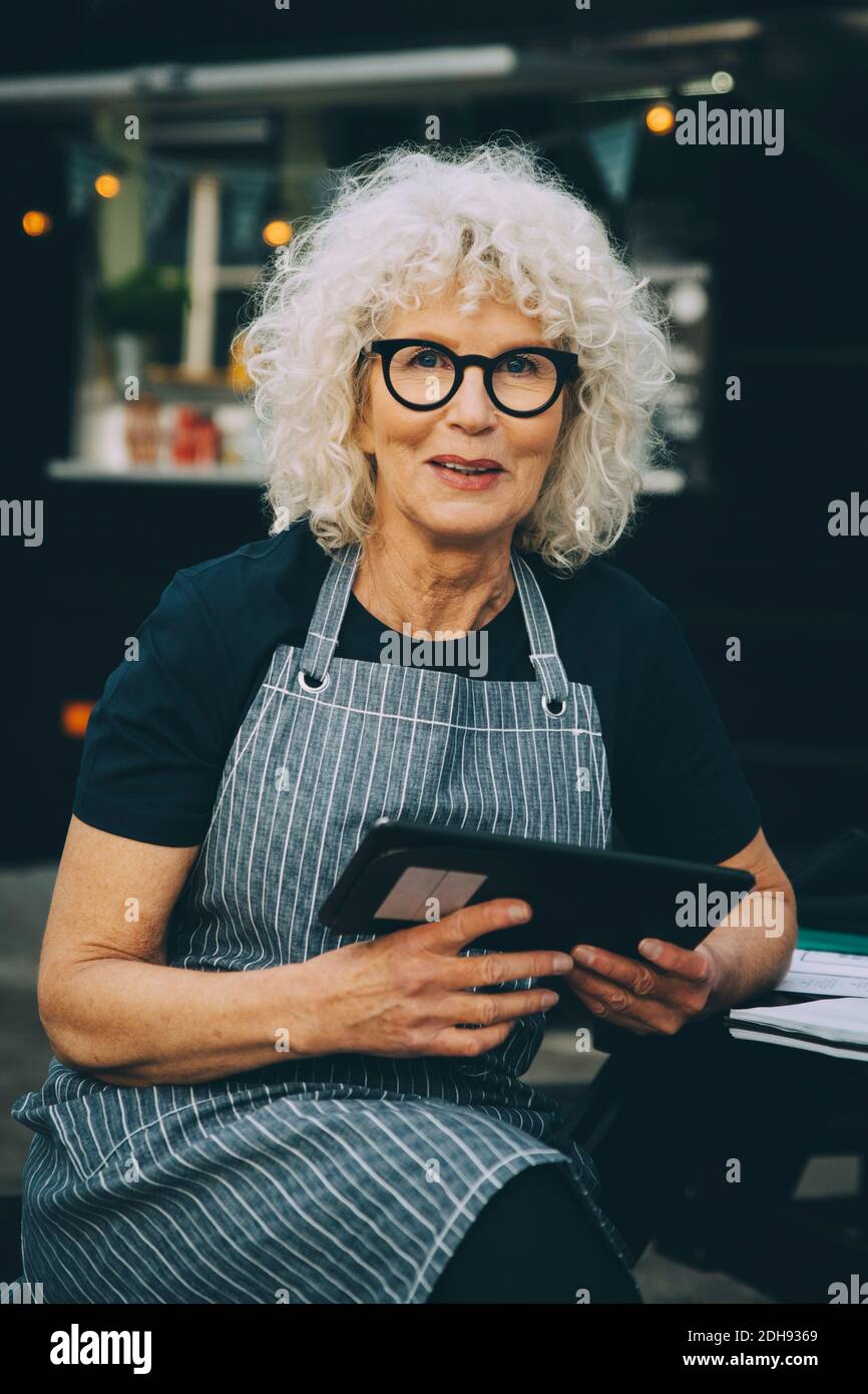 Portrait of senior owner with digital tablet against food truck in city Stock Photo