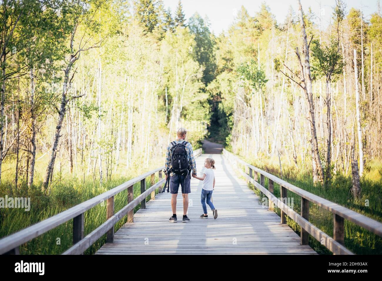 Father with backpack talking to daughter while standing on footbridge in forest Stock Photo