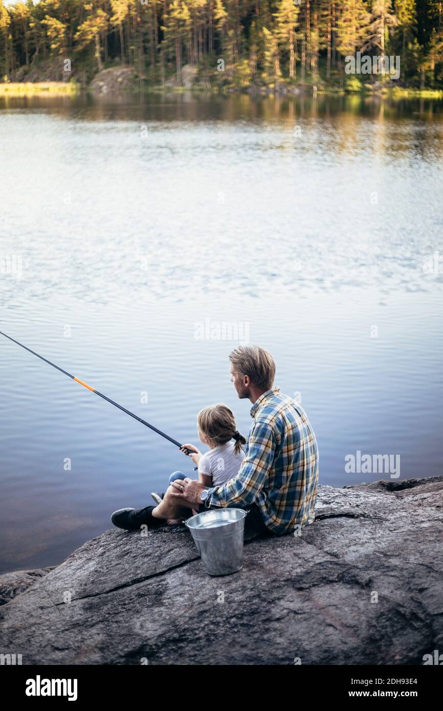 Father and daughter fishing while sitting by lake Stock Photo