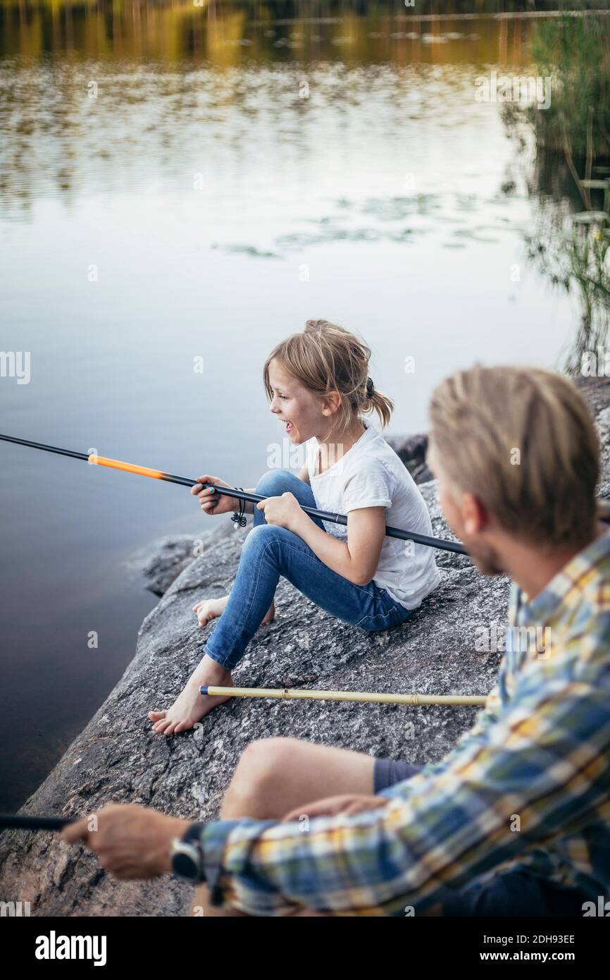 Smiling daughter enjoying fishing with father at lake Stock Photo