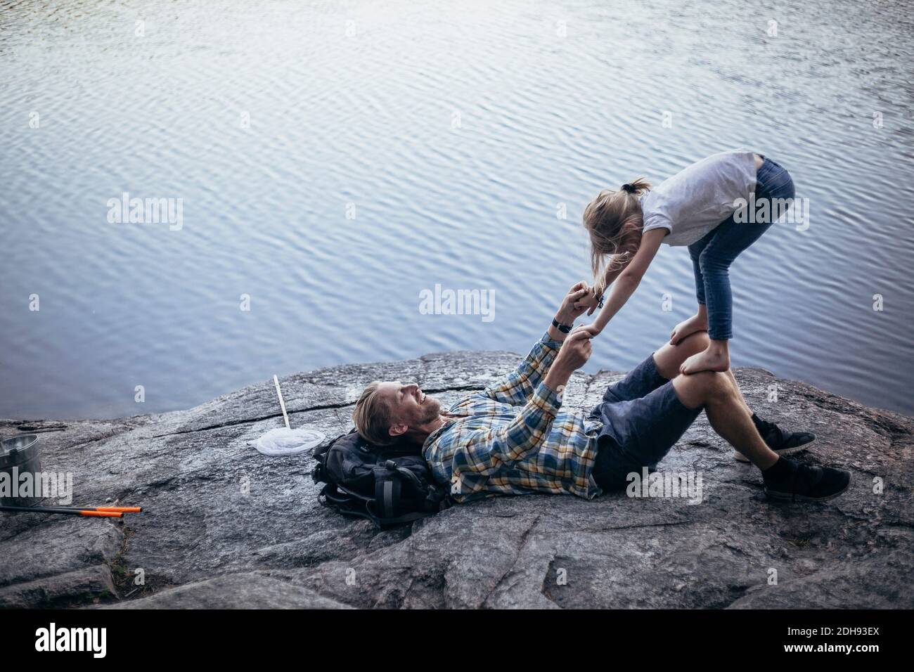 Smiling father playing with daughter while lying down by lake Stock Photo