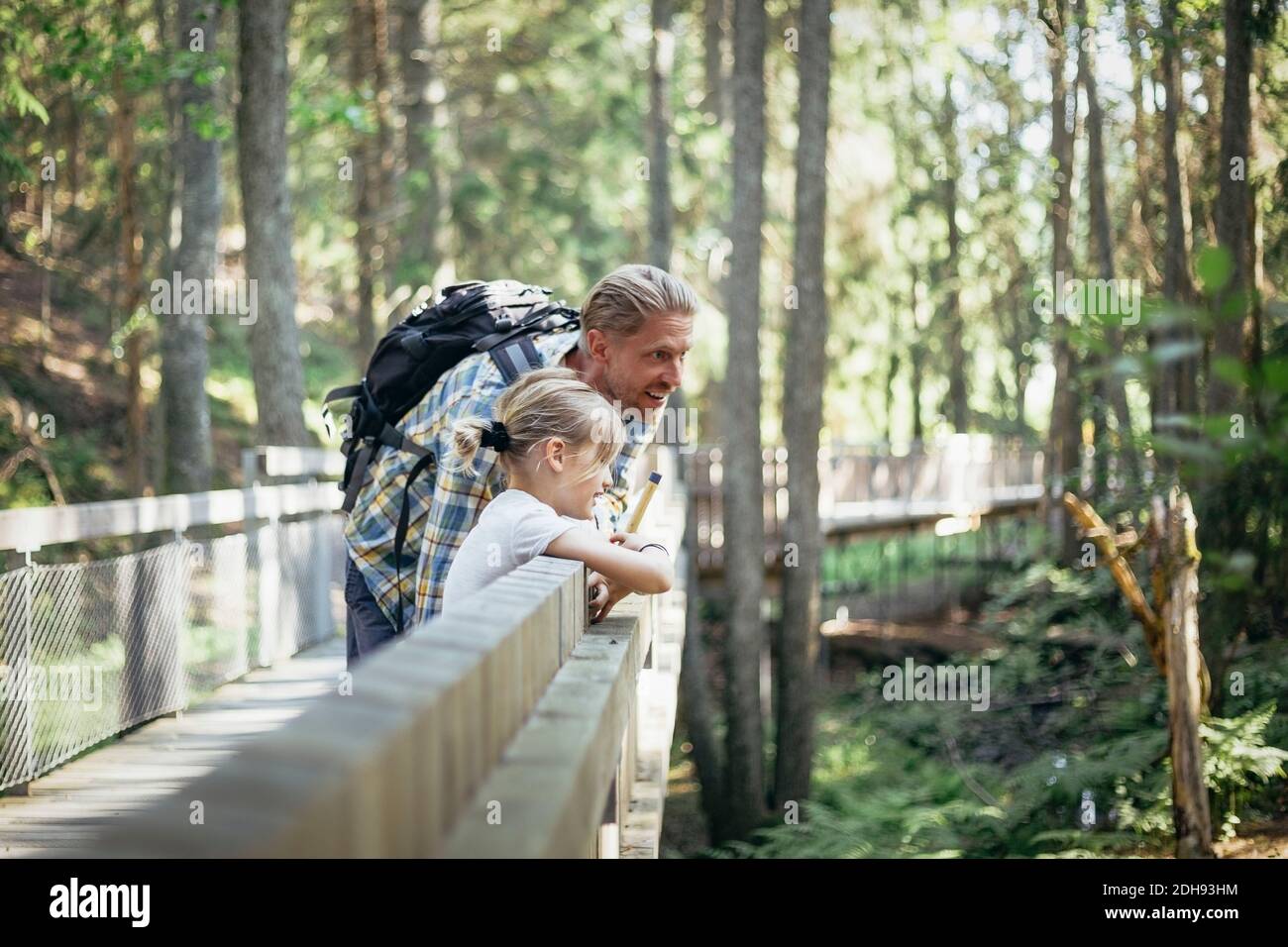 Smiling father with backpack talking to daughter on footbridge in forest Stock Photo