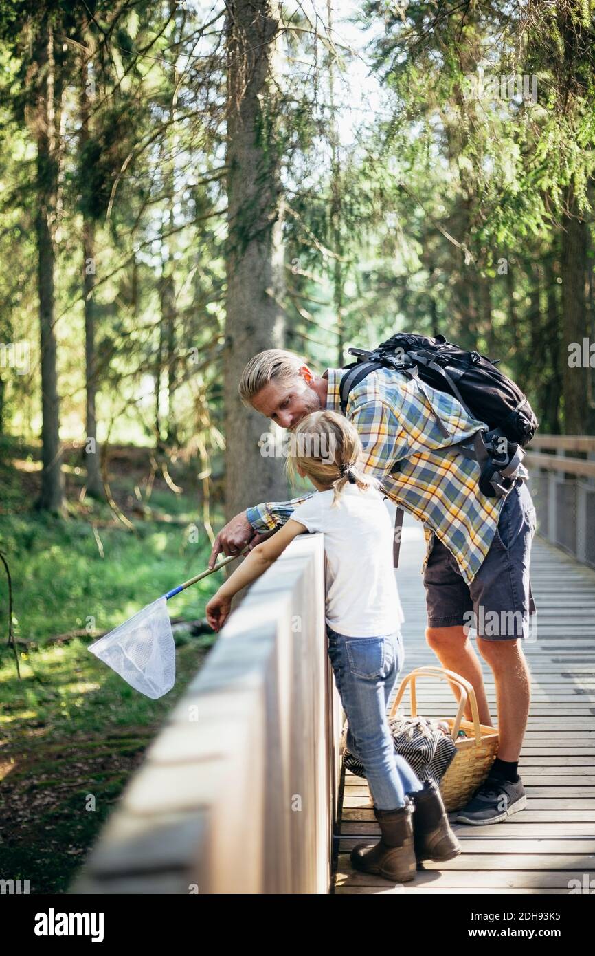 Father with backpack talking to daughter on footbridge in forest Stock Photo