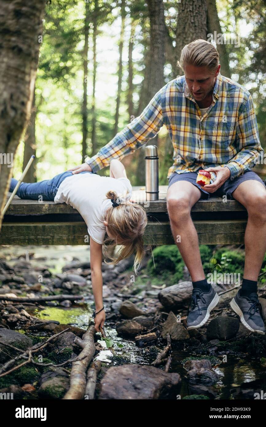 Father with apple holding daughter fishing on footbridge in forest Stock Photo