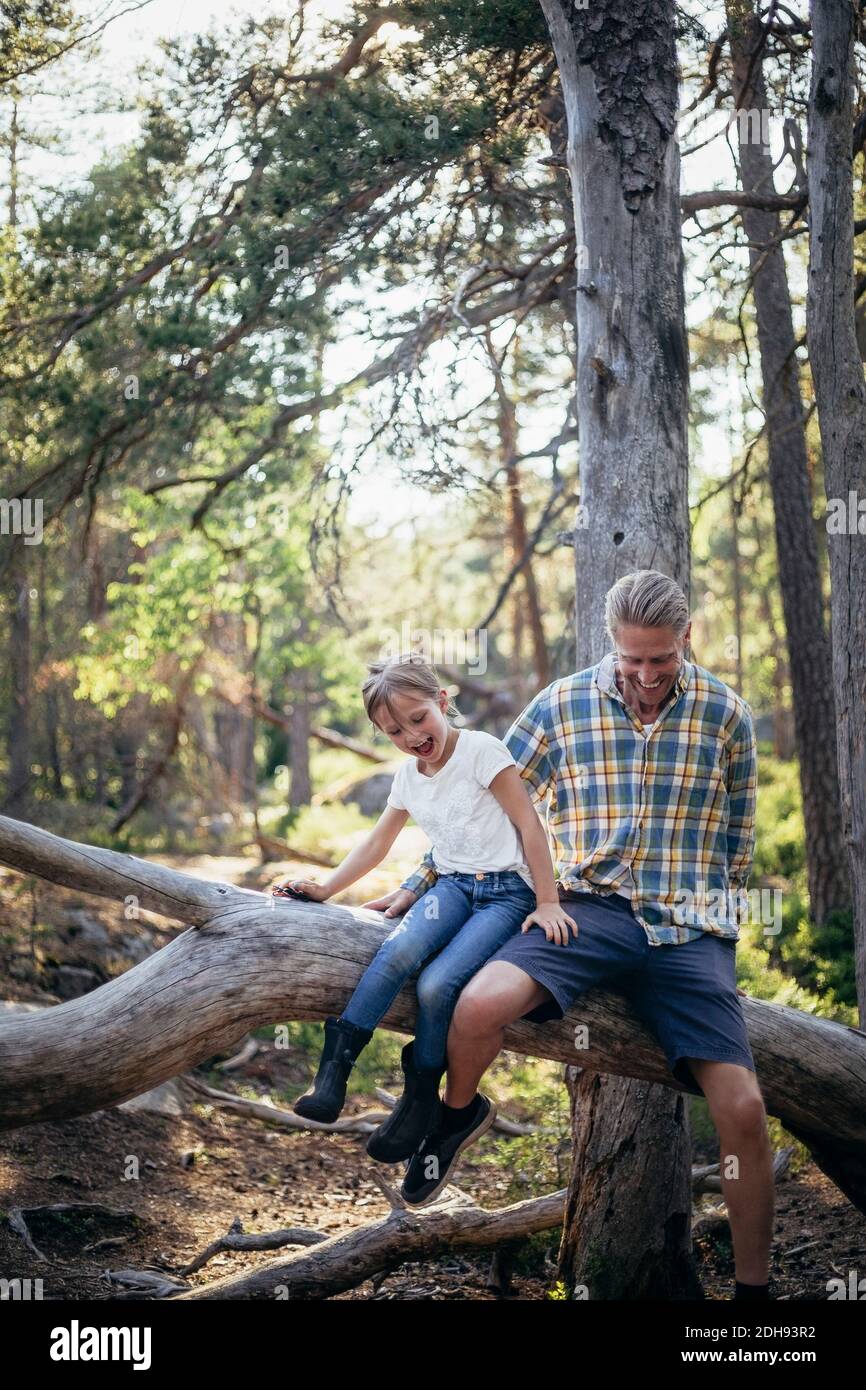 Happy father and daughter moving down on fallen tree in forest Stock Photo