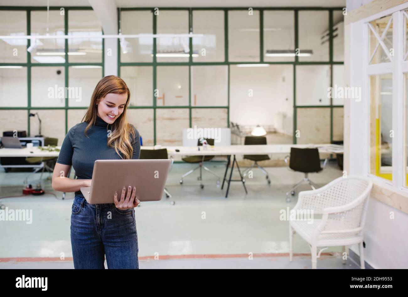 Happy young woman using laptop in creative office Stock Photo