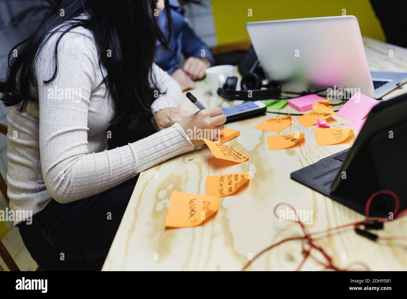 Midsection of young woman writing on adhesive note at wooden desk in office Stock Photo