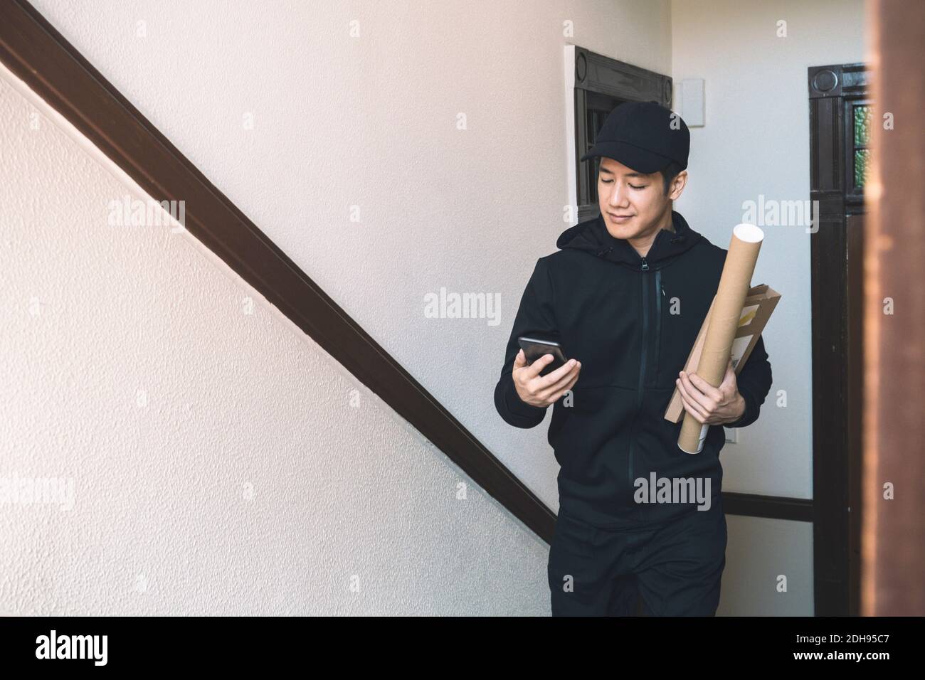 Smiling delivery man with package using phone against wall Stock Photo