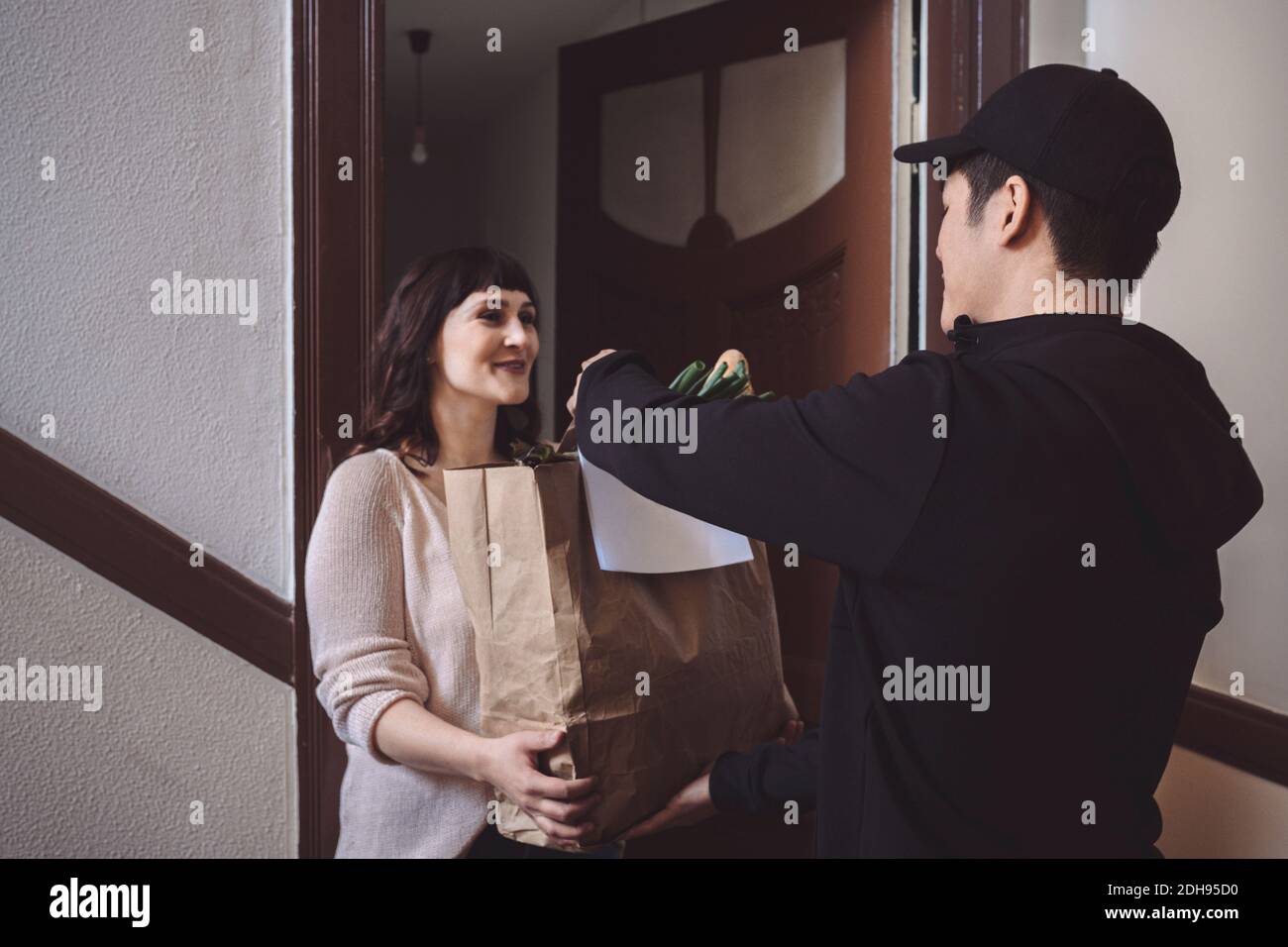 Smiling customer talking to delivery man while holding vegetable bag at doorstep Stock Photo