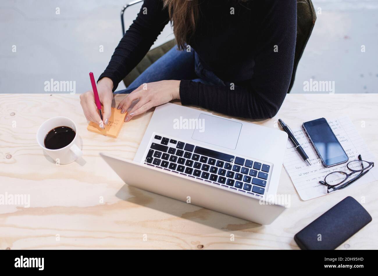 High angle view of young woman writing on adhesive note by laptop at desk Stock Photo