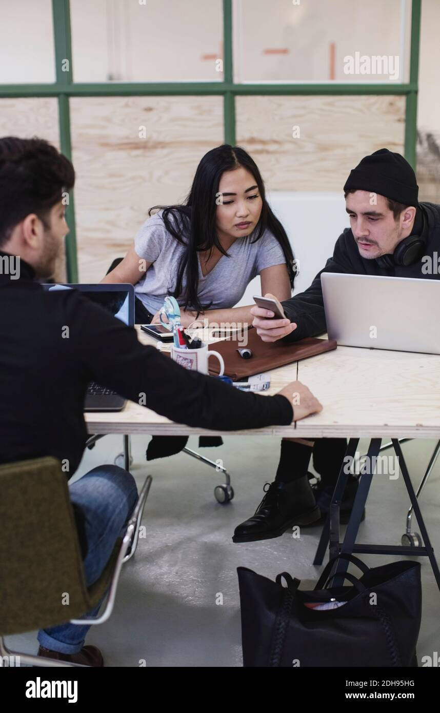 Three colleagues using smart phone at desk in creative office Stock Photo