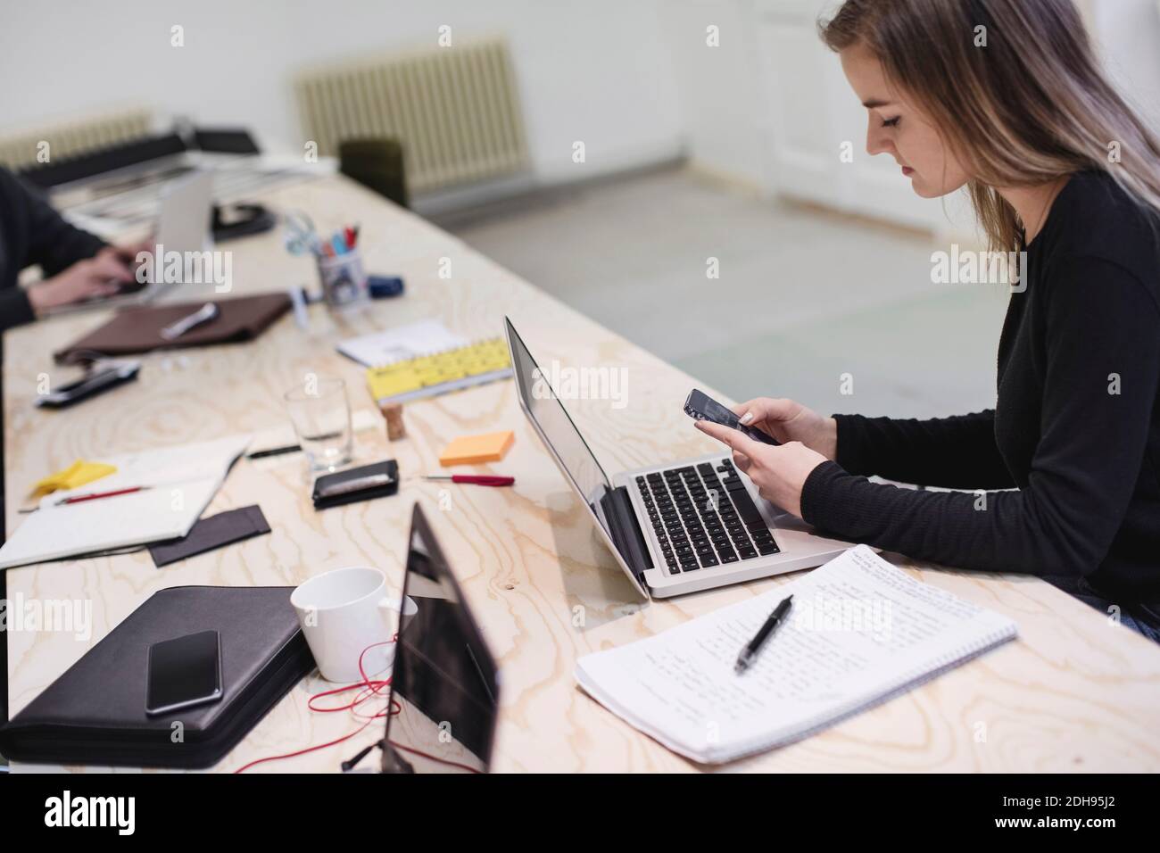 Young woman using smart phone at desk in creative office Stock Photo