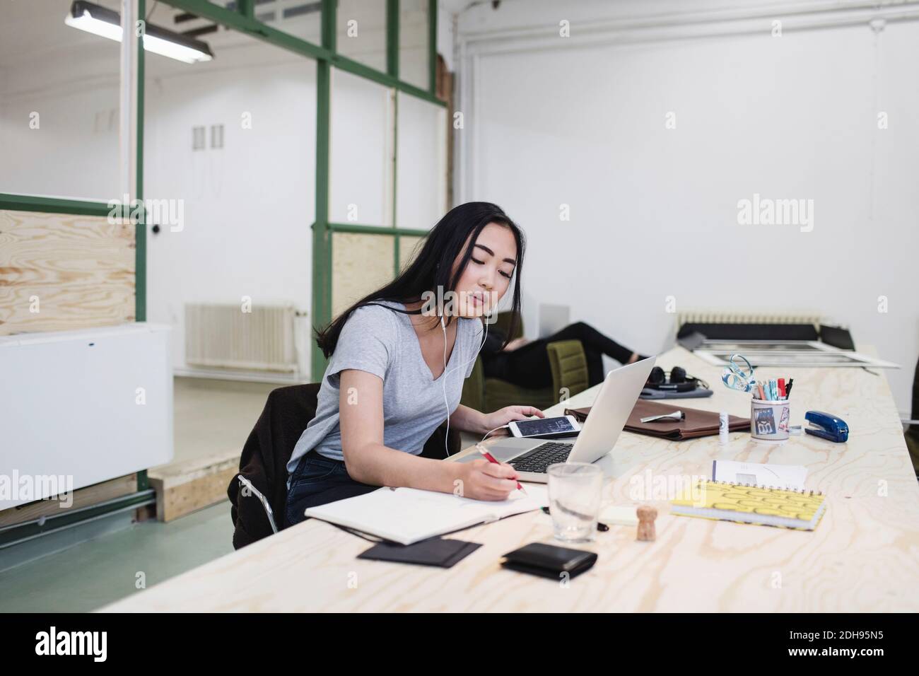 Young woman writing while working at desk in office Stock Photo