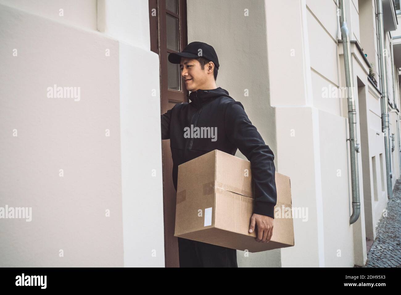 Smiling delivery man with package standing at doorstep Stock Photo