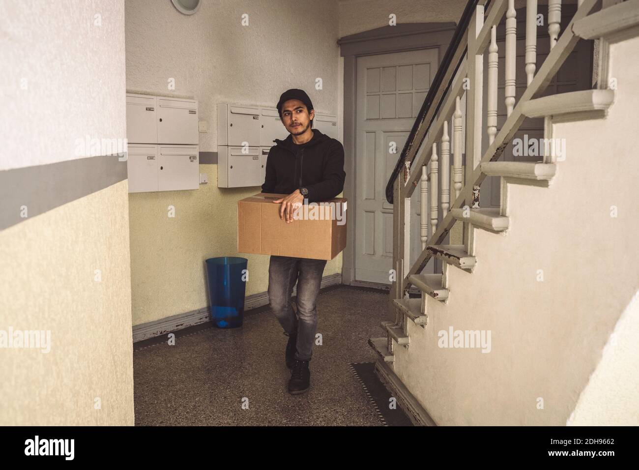 Full length of delivery man with package box walking by staircase Stock Photo