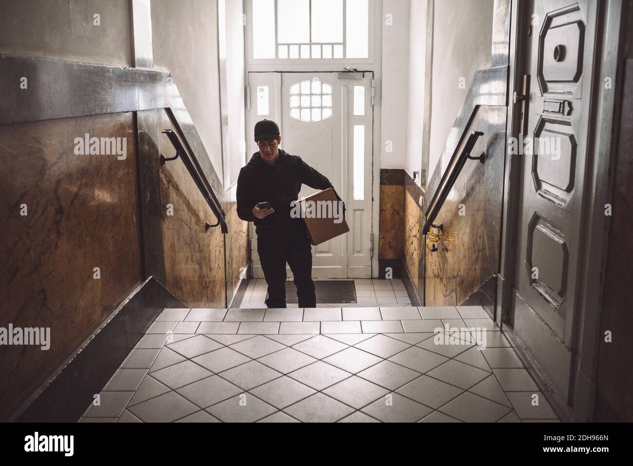 Delivery man with package using mobile phone against door Stock Photo