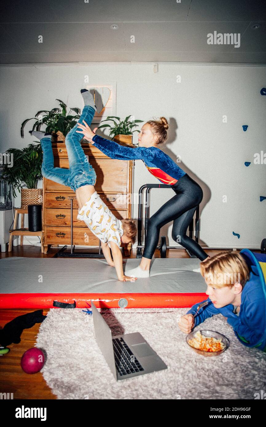 Male and female sibling practicing handstand while brother looking at laptop in living room Stock Photo