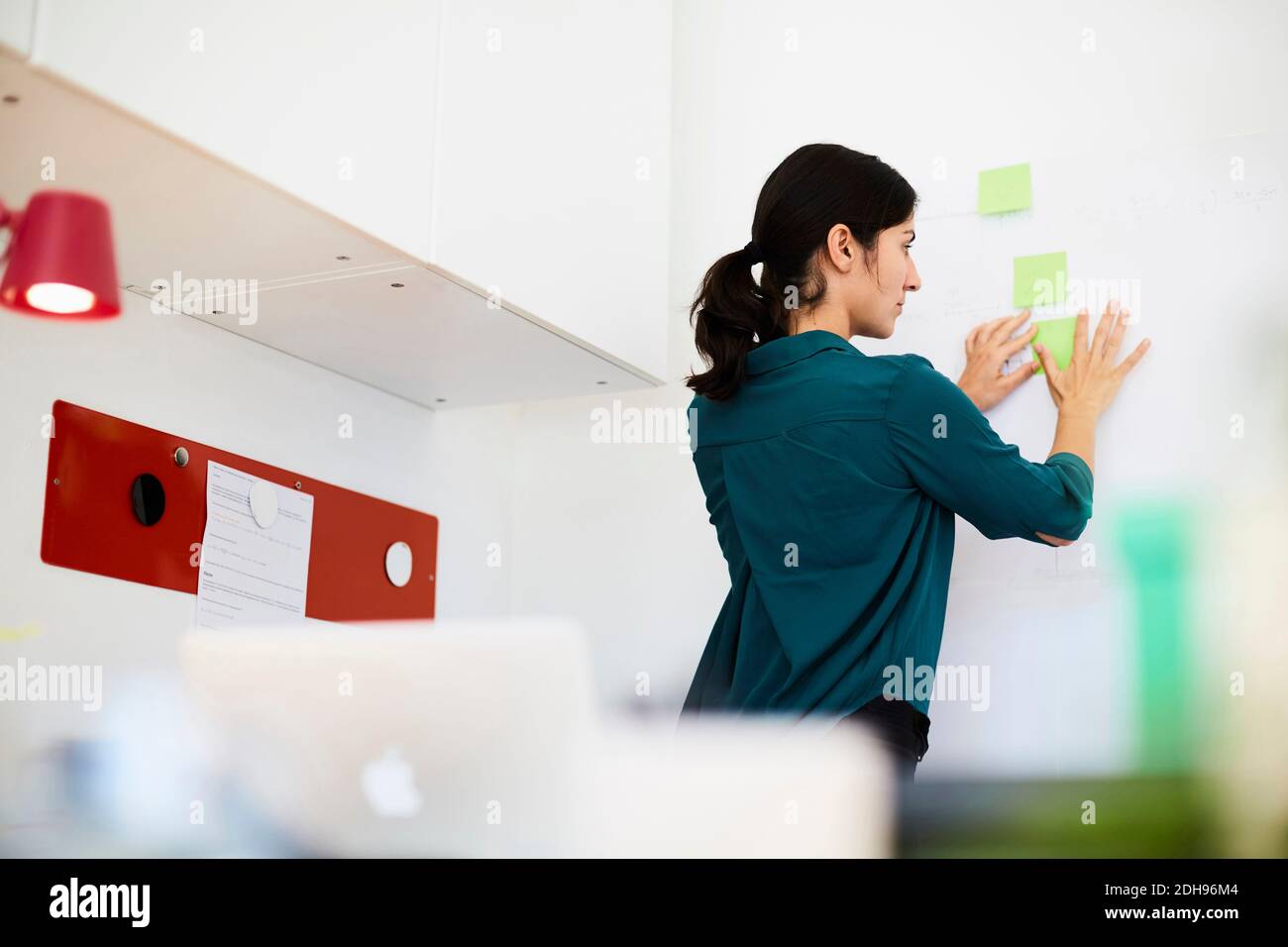 Rear view of mid adult businesswoman placing sticky notes on whiteboard ...