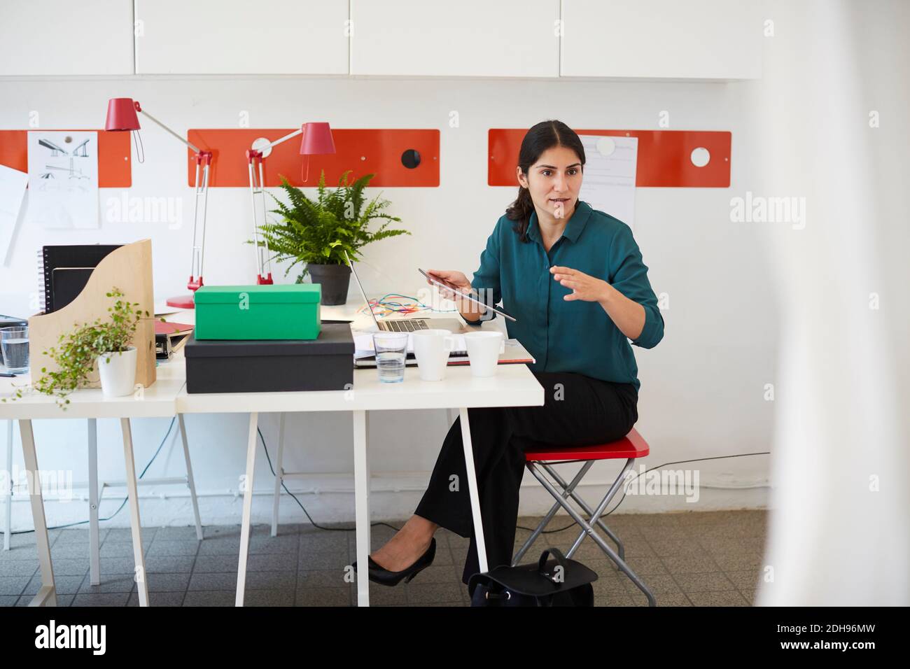 Mid adult businesswoman gesturing while holding digital tablet at table in office Stock Photo